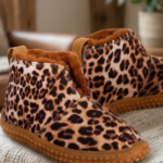Botas bajas de mujer con estampa animal print de leopardo e interior de piel sintética marrón, apoyadas sobre una manta tejida en un ambiente acogedor con chimenea