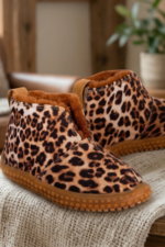 Botas bajas de mujer con estampa animal print de leopardo e interior de piel sintética marrón, apoyadas sobre una manta tejida en un ambiente acogedor con chimenea