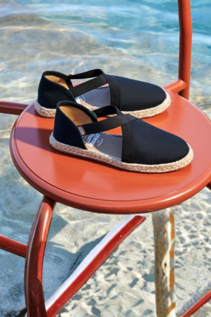 "Sandalia Flex Relic negra de tela con tiras cruzadas y suela de yute trenzado sobre fondo de agua."