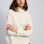 "Mujer vistiendo la Polera Anthony tejida en color negro, off white y gris melange, con cuello alto, hombros caídos y calce holgado sobre pantalón oscuro, marca Agustina Dominguez."