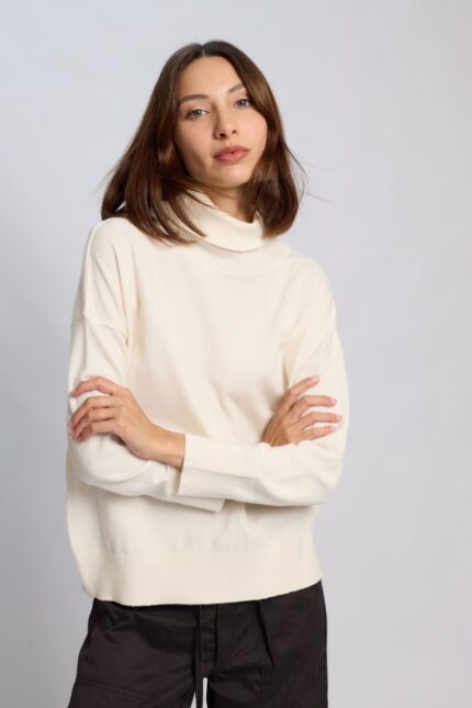 "Mujer vistiendo la Polera Anthony tejida en color negro, off white y gris melange, con cuello alto, hombros caídos y calce holgado sobre pantalón oscuro, marca Agustina Dominguez."