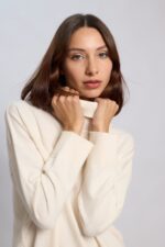 MUjer vistinedo un poleron blanqucino de homrbos caidos y suave texrura