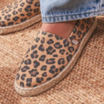 "Alpargatas Chimmy Churry de lona con estampado animal print de leopardo en tonos camel y marrón, sin elástico, con base de yute natural y suela de goma antidespirante, presentadas sobre una mesa de madera rústica."