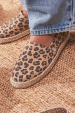 "Alpargatas Chimmy Churry de lona con estampado animal print de leopardo en tonos camel y marrón, sin elástico, con base de yute natural y suela de goma antidespirante, presentadas sobre una mesa de madera rústica."