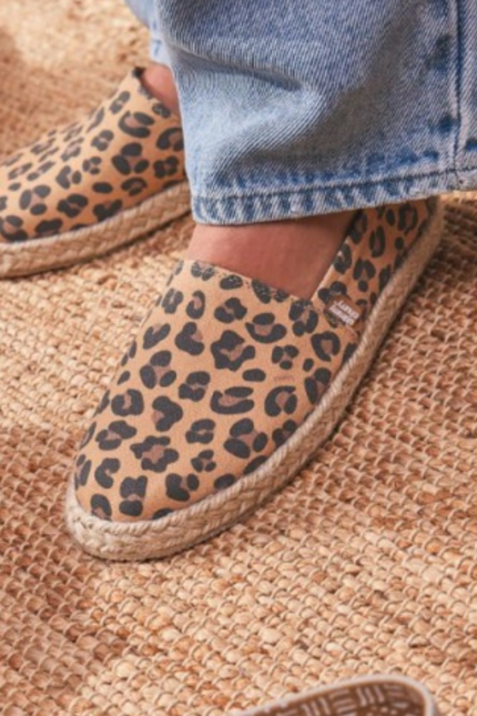 "Alpargatas Chimmy Churry de lona con estampado animal print de leopardo en tonos camel y marrón, sin elástico, con base de yute natural y suela de goma antidespirante, presentadas sobre una mesa de madera rústica."