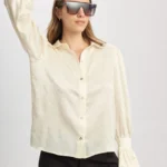 Camisa Coral blanca satinada de Estancias Wear, de silueta recta y mangas largas con puños fruncidos, modelada con pantalones negros y gafas de sol grandes en estudio.