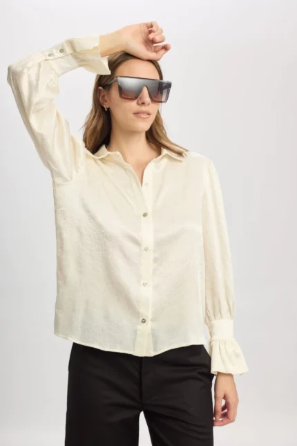 Camisa Coral blanca satinada de Estancias Wear, de silueta recta y mangas largas con puños fruncidos, modelada con pantalones negros y gafas de sol grandes en estudio.