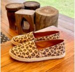 "Alpargatas Chimmy Churry de lona con estampado animal print de leopardo en tonos camel y marrón, sin elástico, con base de yute natural y suela de goma antidespirante, presentadas sobre una mesa de madera rústica."
