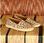 "Alpargatas Chimmy Churry de lona con estampado animal print de leopardo en tonos camel y marrón, sin elástico, con base de yute natural y suela de goma antidespirante, presentadas sobre una mesa de madera rústica."