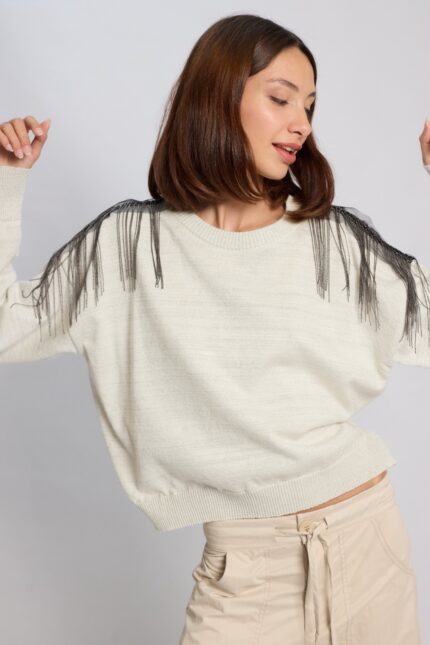 Modelo posando de frente con el Sweater Benedetti de Vanesa Petris en color crudo con lúrex y flecos de cadenas negras en los hombros.