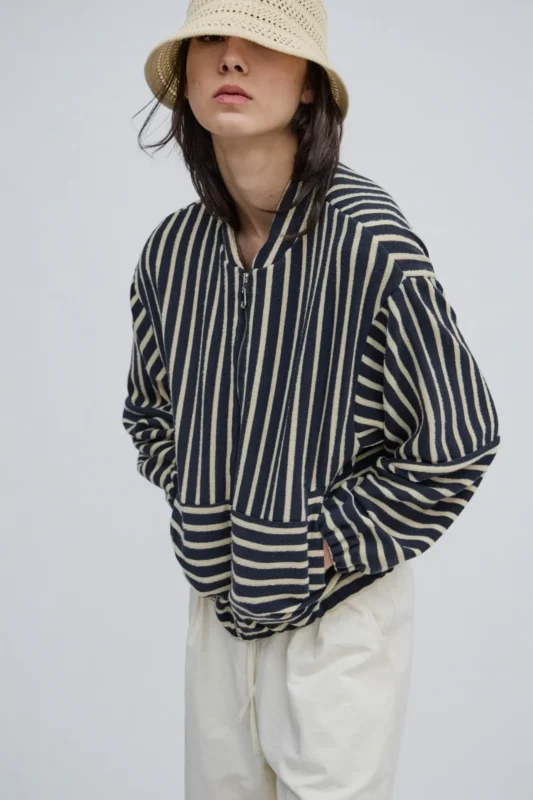 Campera bomber rayada azul marino y crudo en tejido de punto oversize combinada con pantalón claro.